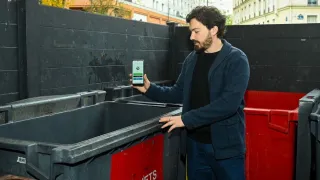 A man standing next to a trash container showing his phone