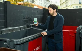 A man standing next to a trash container showing his phone