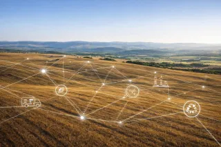 Aerial view of a sunlit rural landscape overlaid with a network of connecting lines and icons representing transport, agriculture, industry and recycling, illustrating a transparent, circular supply-chain system.