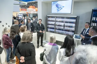 Magnotherm CEO Timur Sirman presents the company's ECLIPSE cooling unit, integrated into a HAUSER RENIMAG refrigerated cabinet stocked with bottled drinks, to a crowd of attendees at the EuroShop 2026 trade fair.